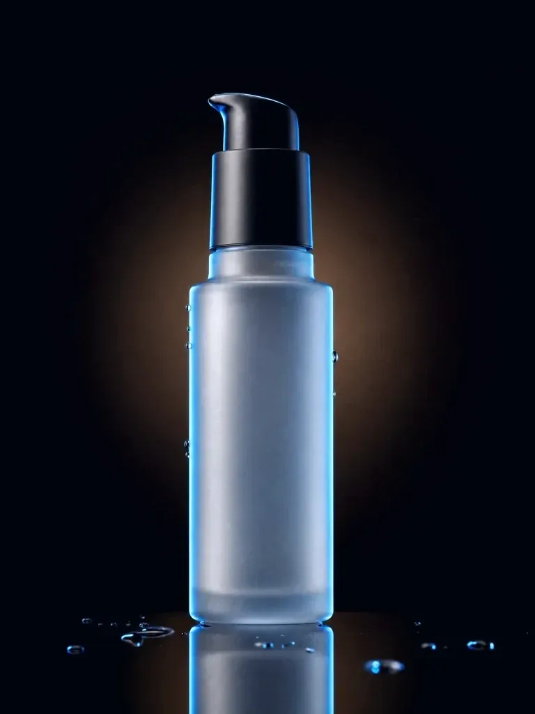 A frosted pump bottle lit by a warm rim light against black, water droplets around its base